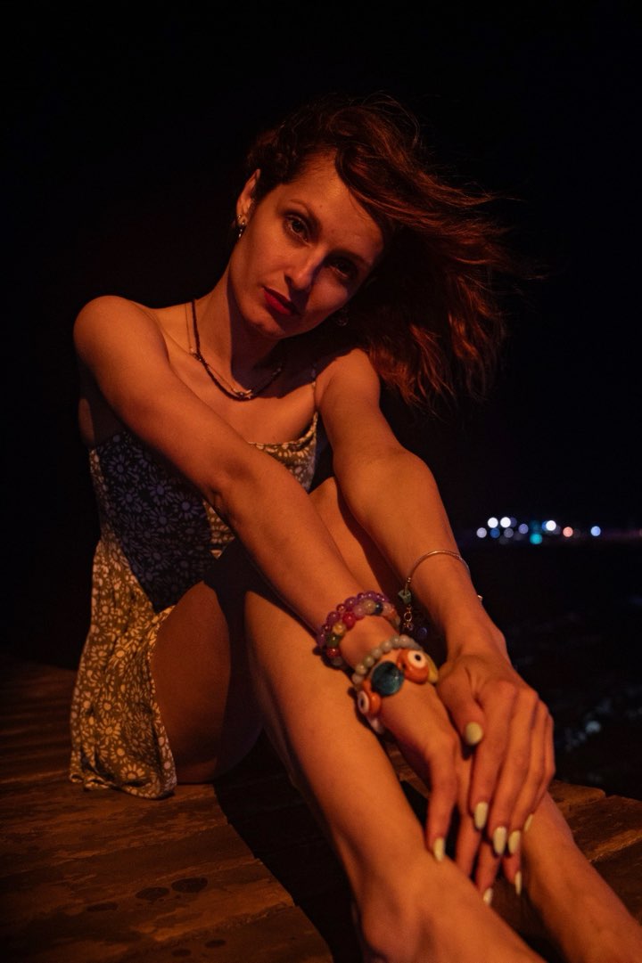Seated portrait by the water at night with colourful bracelets